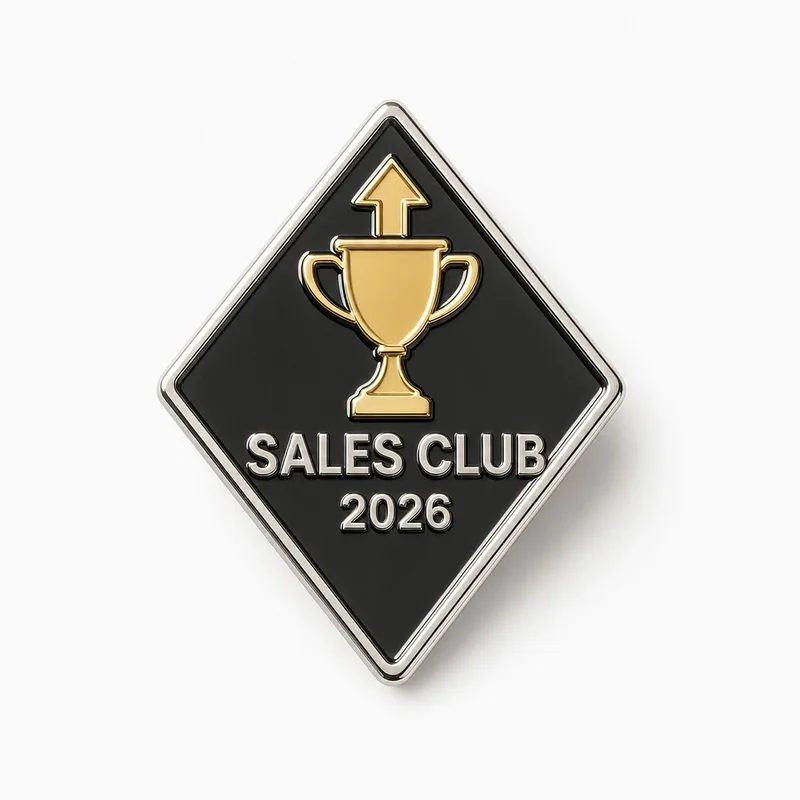 Pin ilustrativo de esmalte duro en forma de rombo, plateado y negro, con un trofeo dorado y una flecha hacia arriba con el texto SALES CLUB 2026