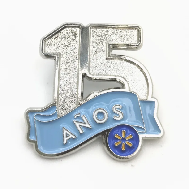 Pin plateado con brillantina, el número 15 y una cinta azul que dice “años”, hecho para los premios por antigüedad de una cadena minorista.