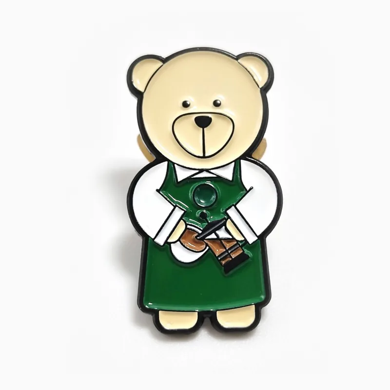 Pin de esmalte de un osito de peluche con delantal verde de barista, hecho para una cadena de cafeterías.