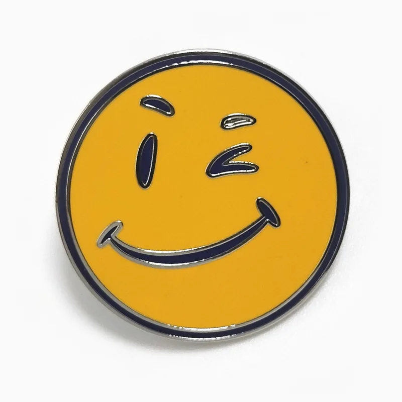 Pin redondo de esmalte amarillo con una carita sonriente que guiña el ojo, hecho para una cadena minorista.