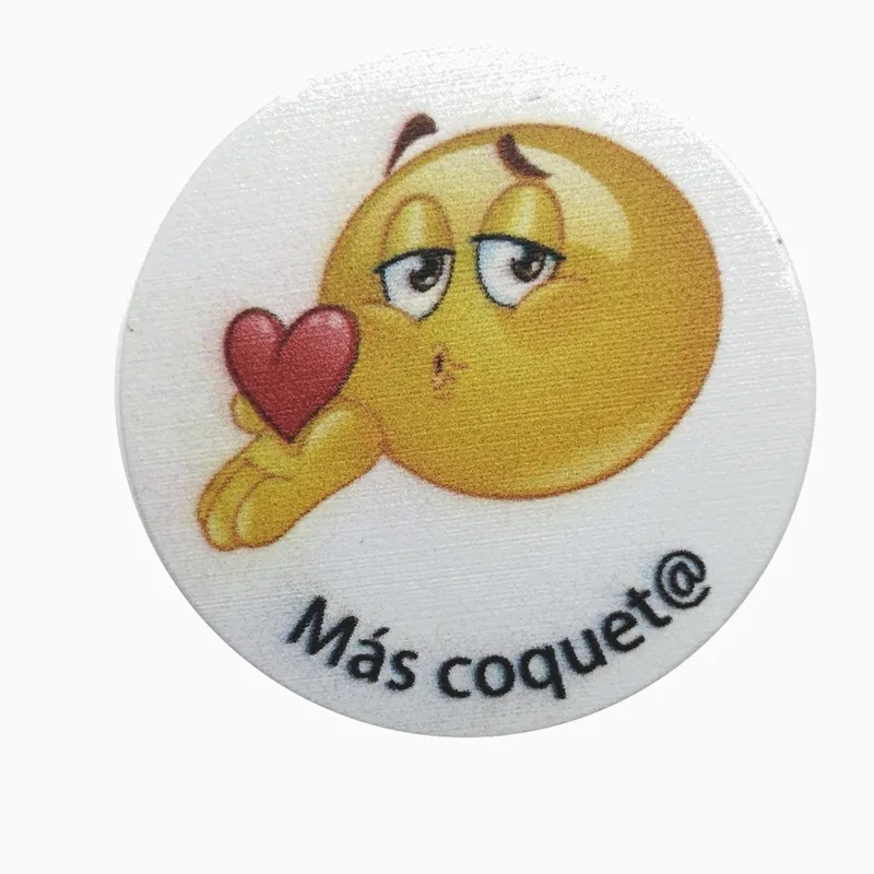 Pin redondo con impresión UV de un emoji guiñando un ojo y el texto Más coquet@ sobre fondo blanco