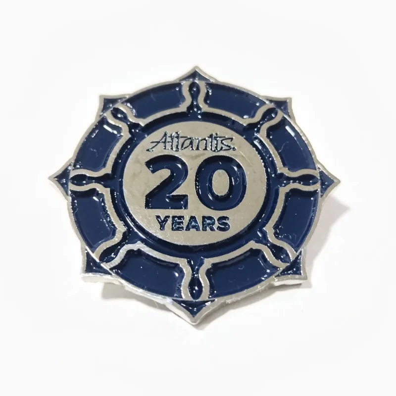 Pin troquelado de níquel con esmalte azul marino y un borde estilo timón alrededor del centro «20 Years» en relieve, con un pequeño logotipo.