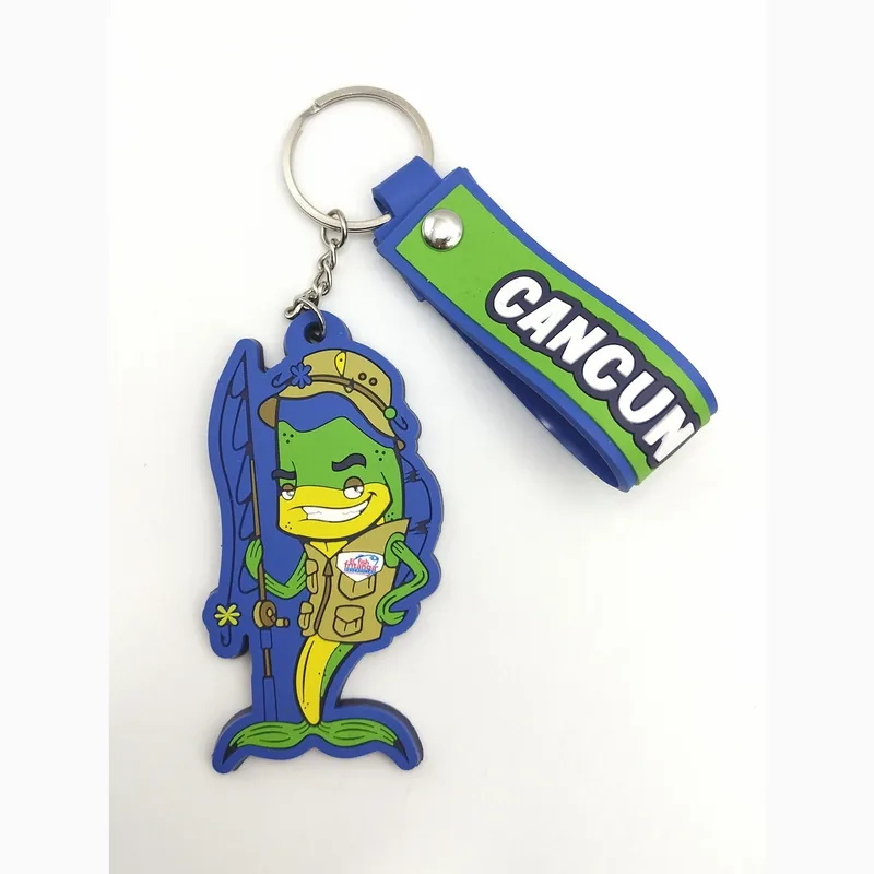 Llavero souvenir de Cancún en PVC suave con un dije de pez pescador caricaturesco y una correa azul y verde con el texto CANCUN, en una argolla.